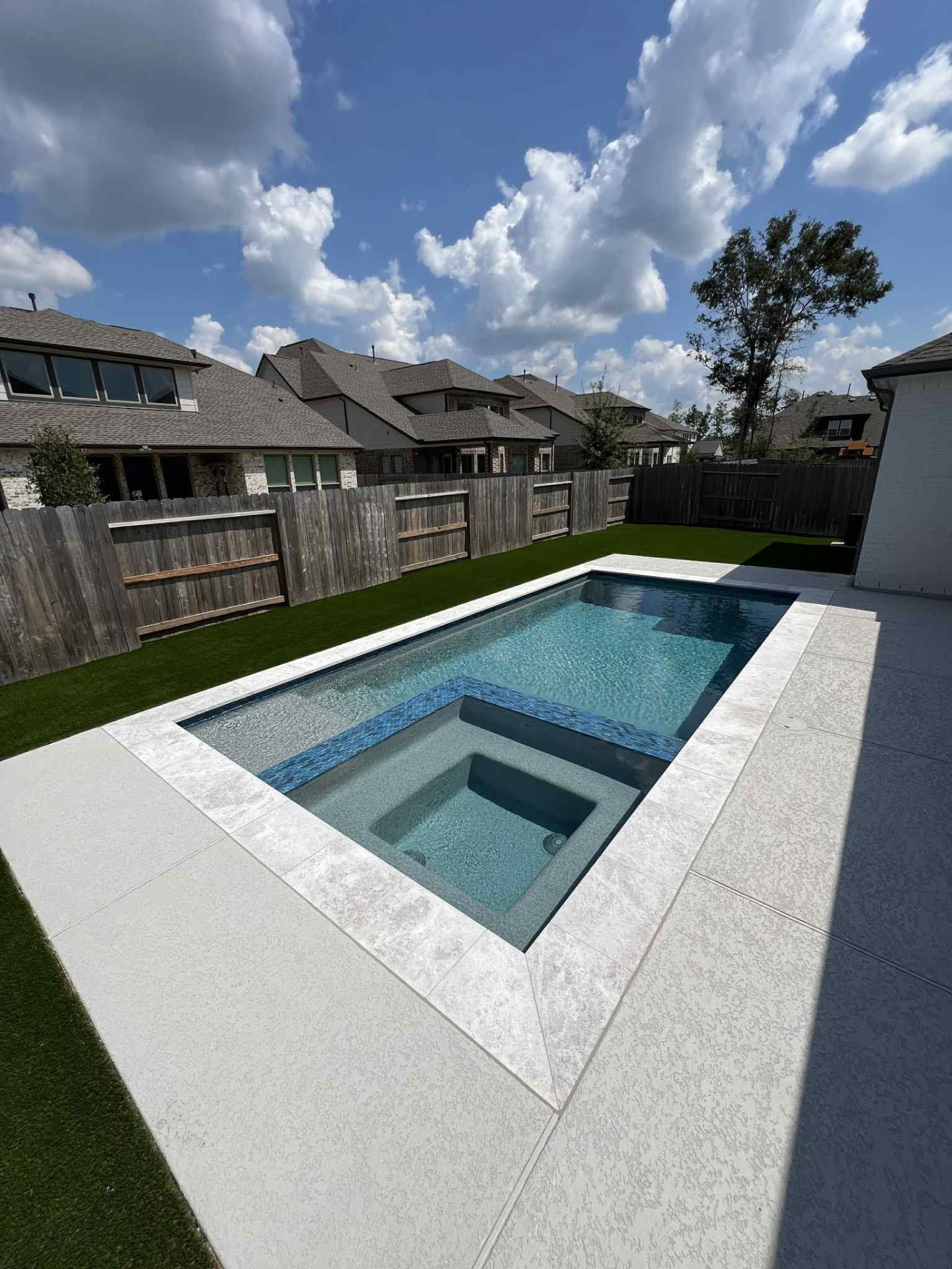Geometric pool and spa with marble coping and turf lawn
