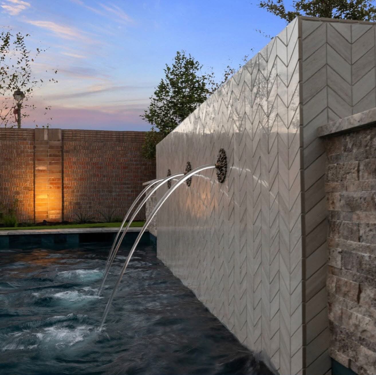 Close-up of deck jets arcing from a chevron tile water wall into a pool at dusk