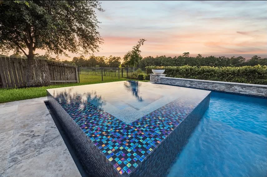Raised spa with iridescent glass mosaic tile spilling into a pool at sunset