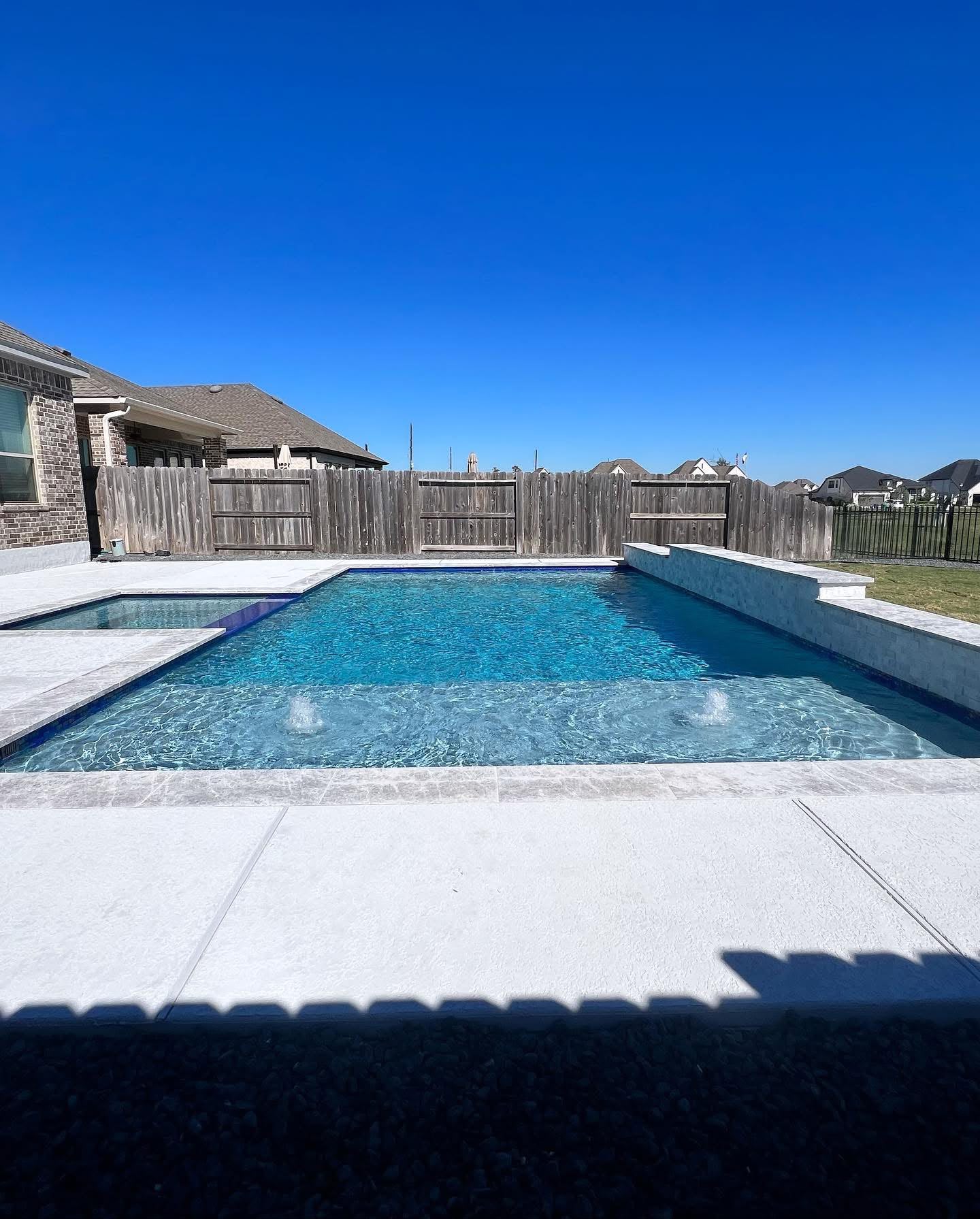 Modern rectangular pool with spa and light travertine decking