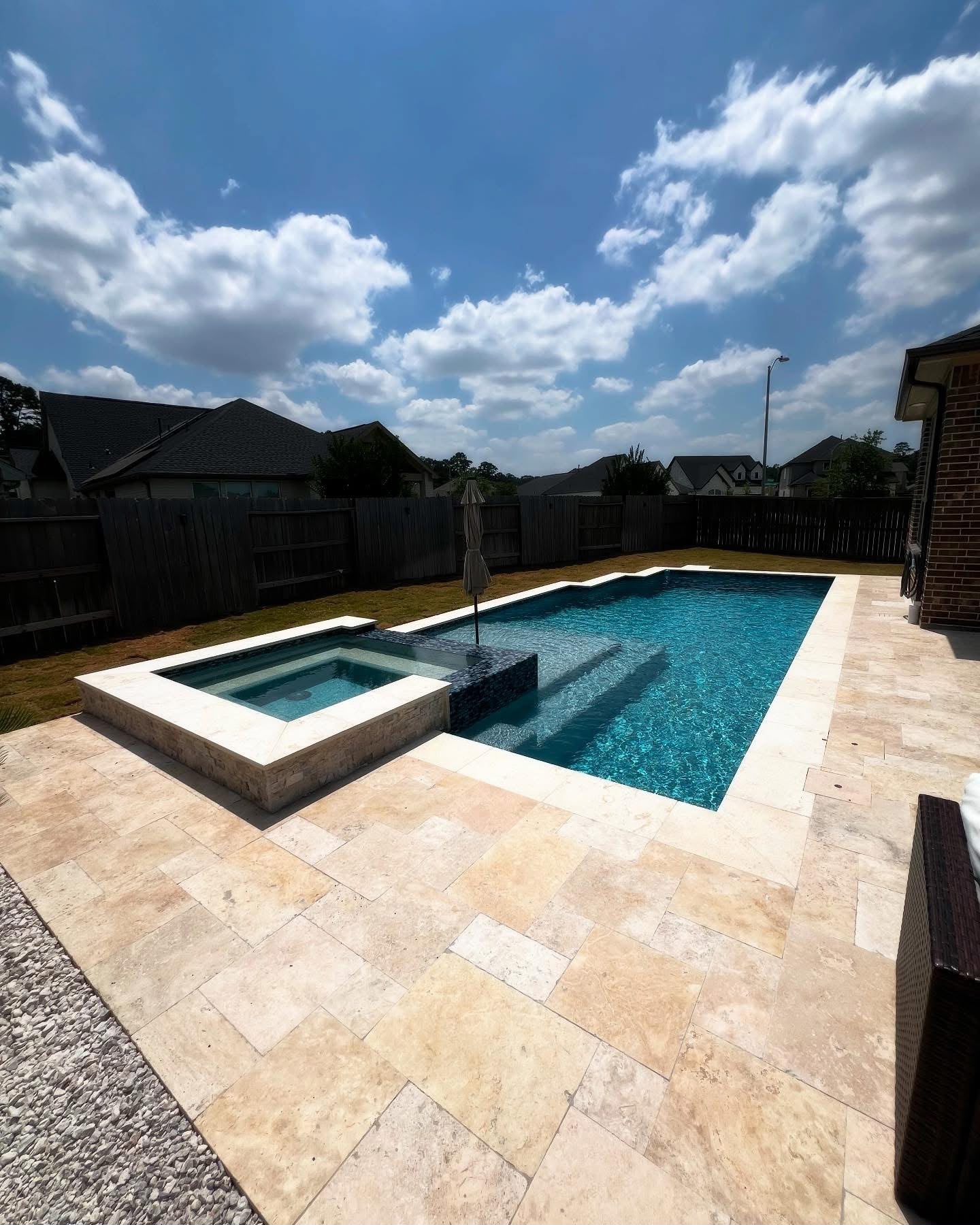 Rectangular pool and raised spa with travertine paver decking